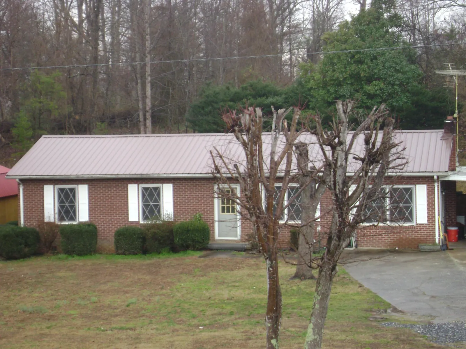 Mauve metal roof on a brick ranch home behind bare trees in Manchester